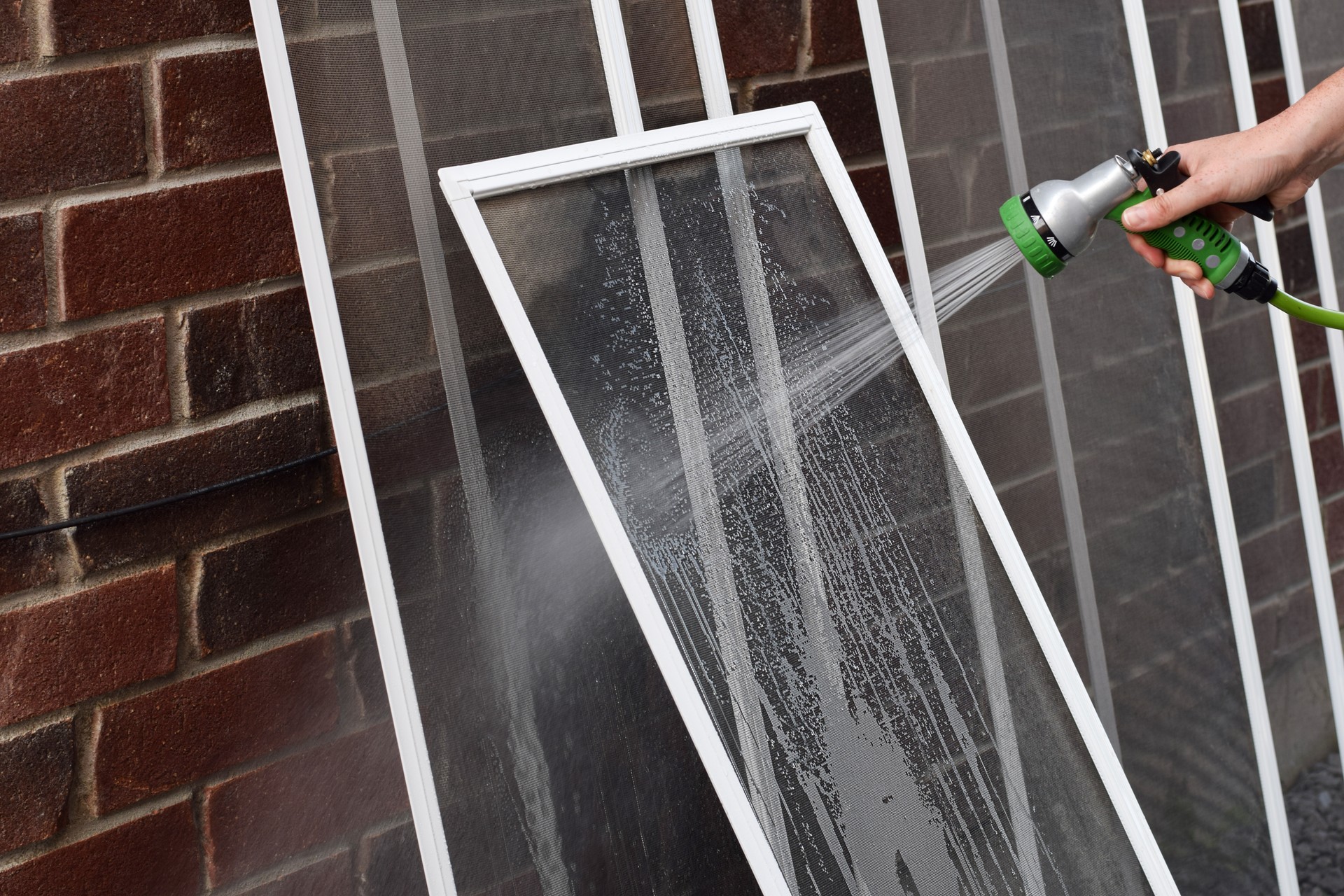 Closeup hand of a person washing dirty window screens with water hose